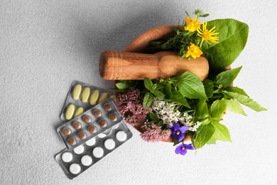 Photo of Wooden mortar with fresh herbs, flowers and pills on white table, flat lay
