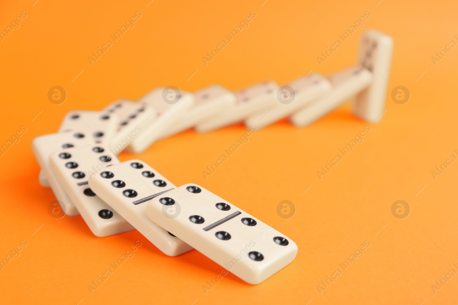 Photo of White domino tiles falling on orange background