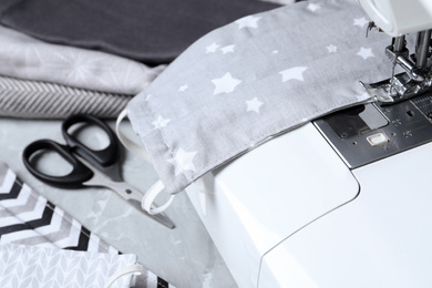 Photo of Sewing machine with homemade protective mask on table, closeup