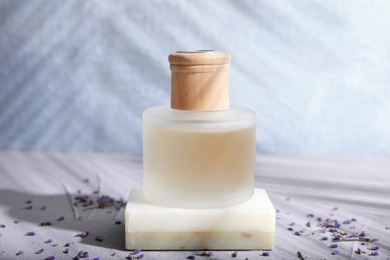 Photo of Bottle with natural lavender oil and soap on table against blurred background
