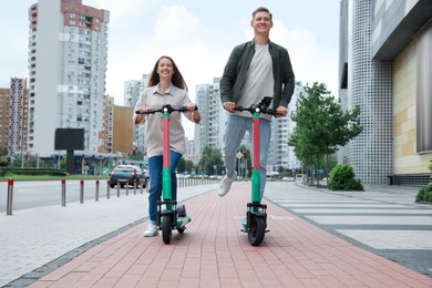 Happy couple riding modern electric kick scooters on city street