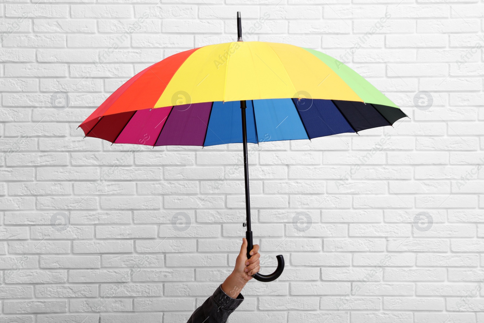 Photo of Woman with open bright umbrella near white brick wall, closeup