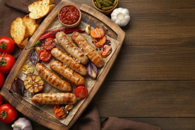 Photo of Tasty grilled sausages and products on wooden table, flat lay. Space for text