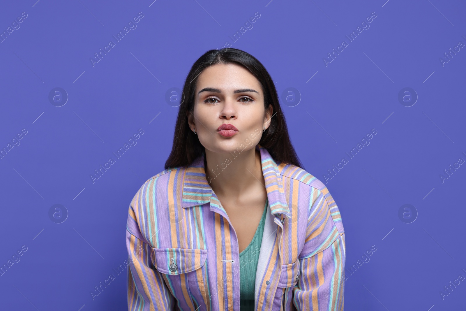 Photo of Beautiful young woman giving kiss on purple background