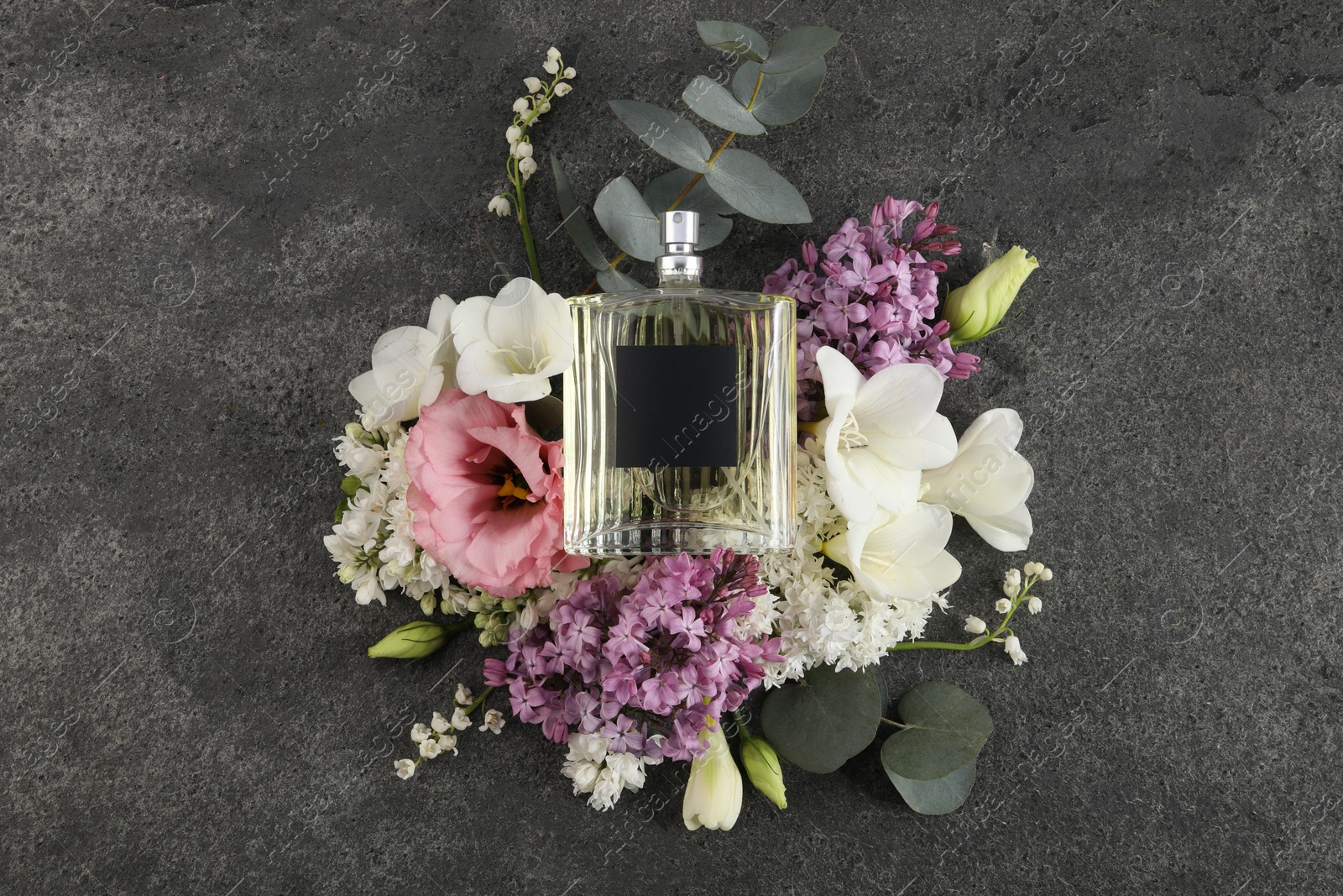 Photo of Bottle of luxury perfume and floral decor on dark grey table, top view