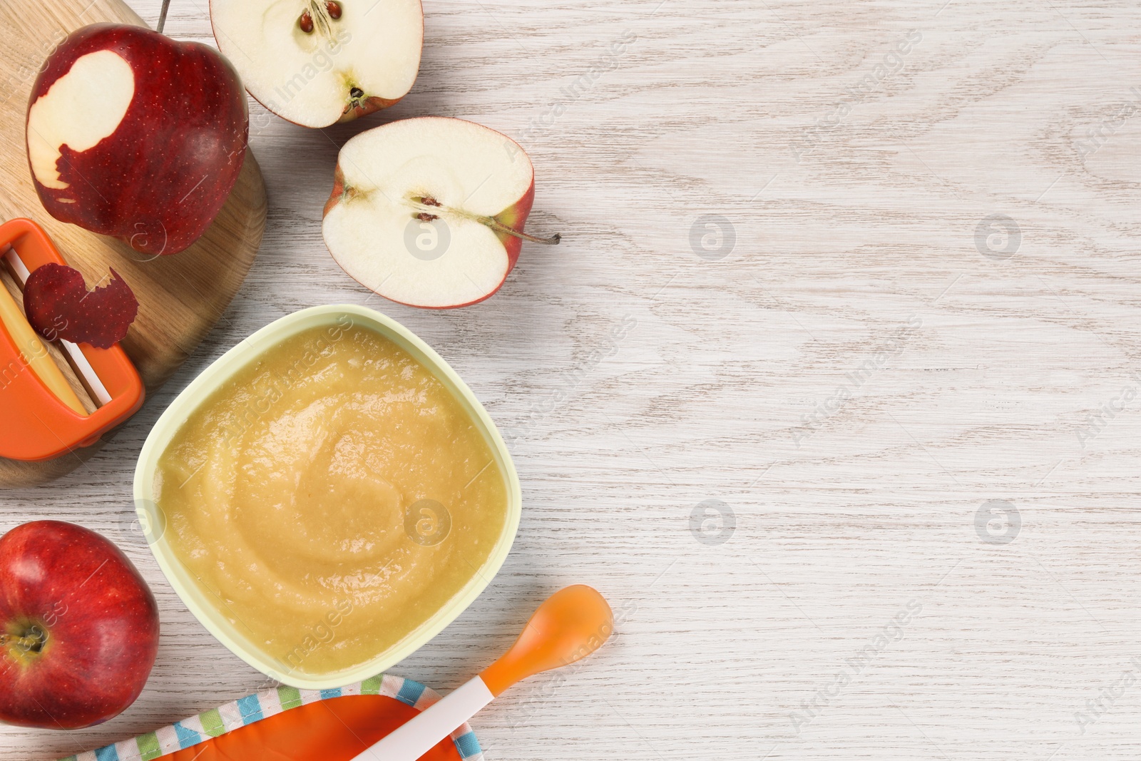 Photo of Healthy baby food. Bowl with delicious apple puree and fresh fruits on white wooden table, flat lay. Space for text