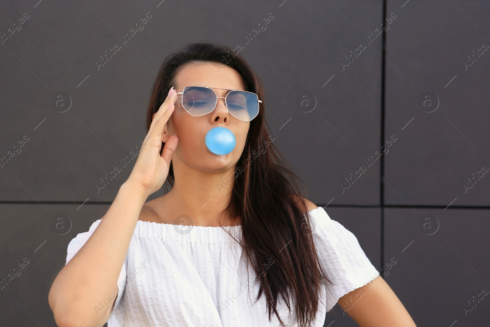 Photo of Beautiful woman blowing gum near dark tiled wall