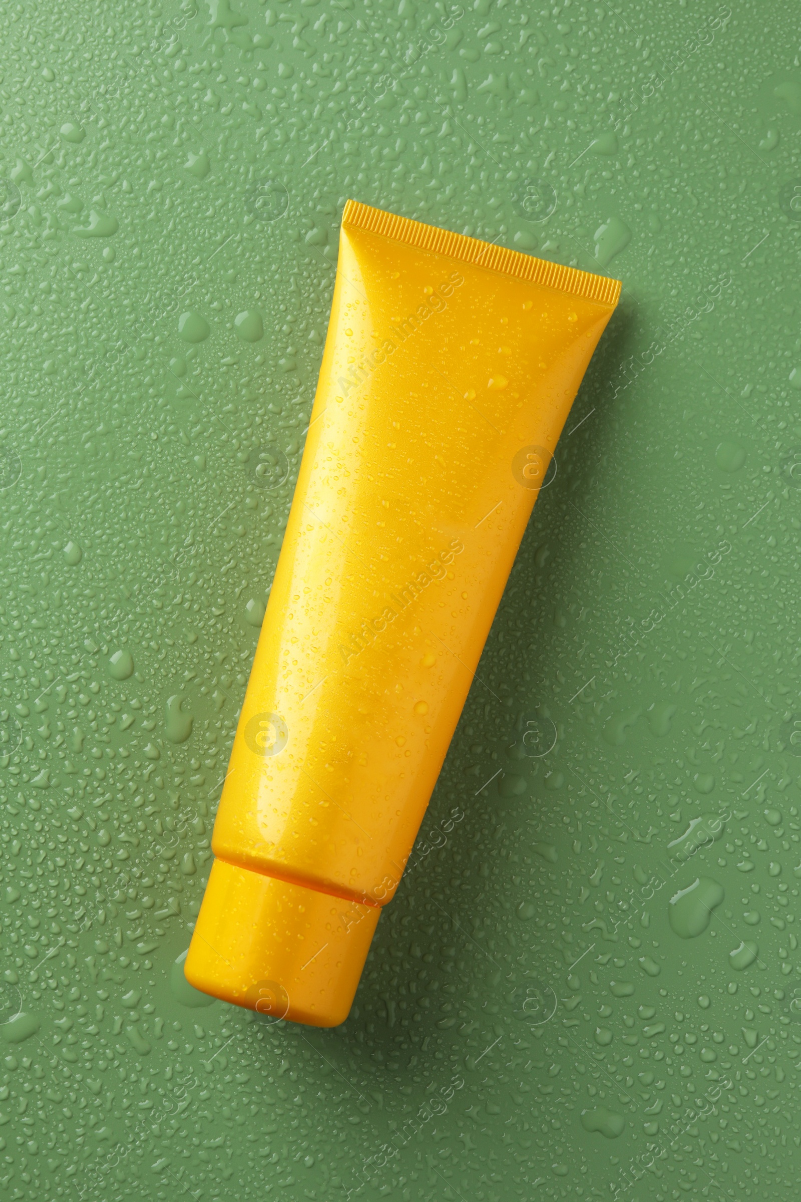 Photo of Moisturizing cream in tube on green background with water drops, top view