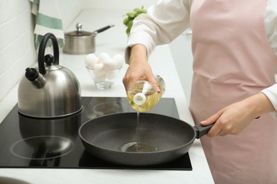 Woman pouring cooking oil from bottle into frying pan in kitchen, closeup