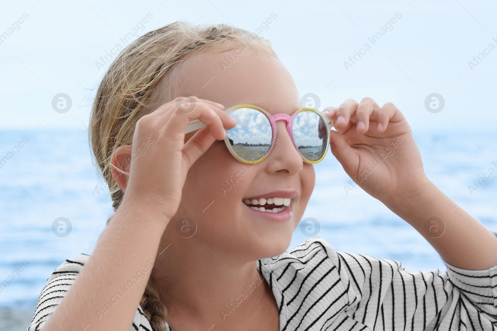 Photo of Little girl wearing sunglasses at beach on sunny day