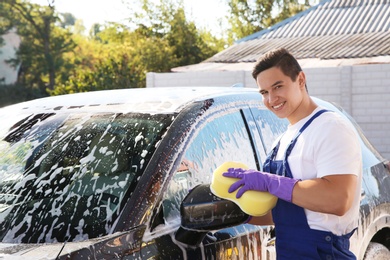 Photo of Worker cleaning automobile with sponge at car wash