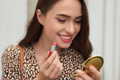 Photo of Beautiful young woman with cosmetic pocket mirror applying lipstick outdoors, closeup