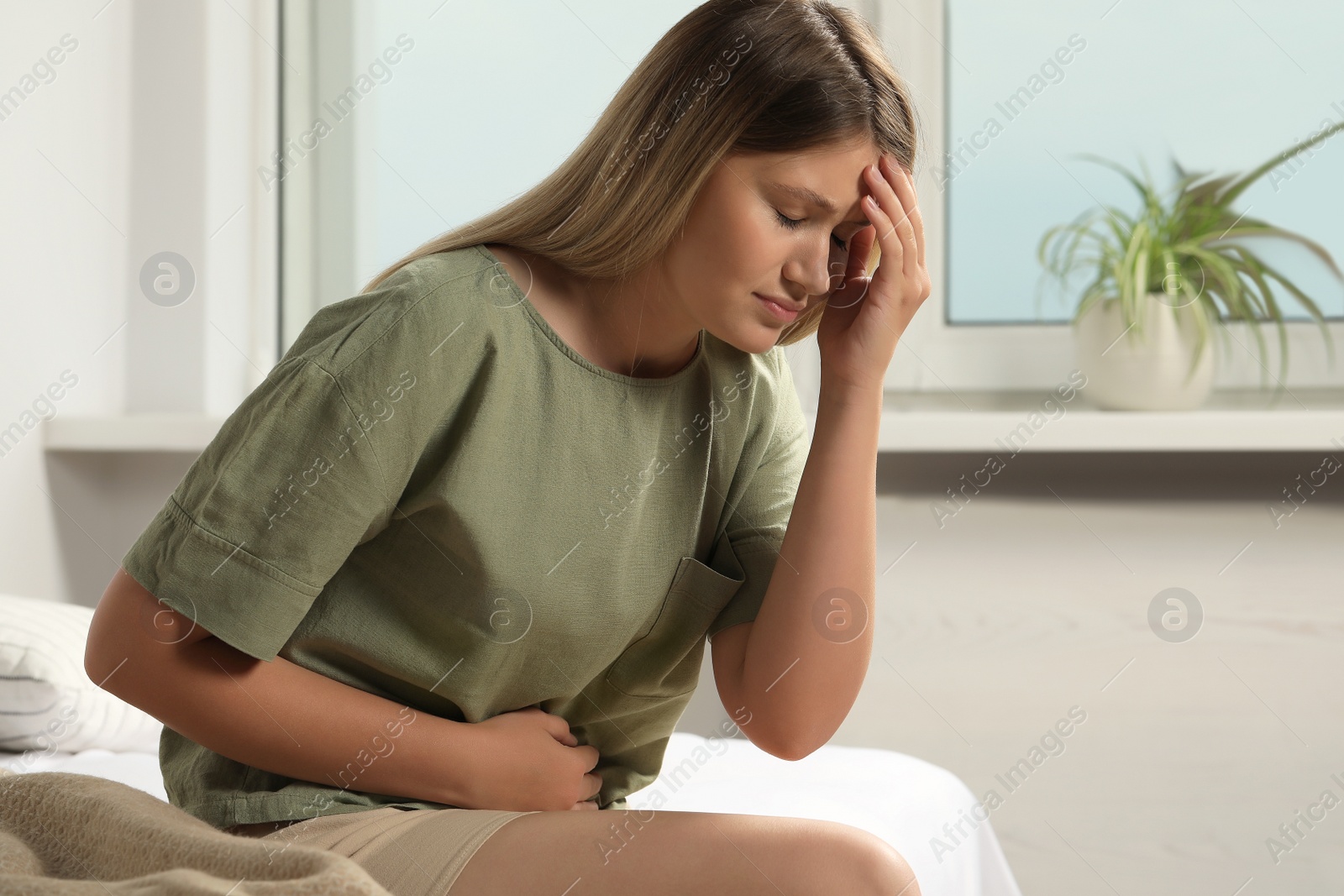 Photo of Young woman suffering from menstrual pain on bed at home