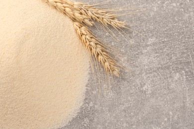 Photo of Pile of uncooked organic semolina and spikelets on grey table, flat lay. Space for text