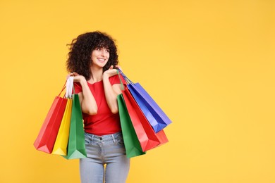 Photo of Happy young woman with shopping bags on yellow background. Space for text