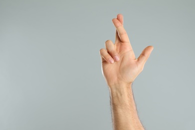 Photo of Man with crossed fingers and space for text on grey background, closeup. Superstition concept