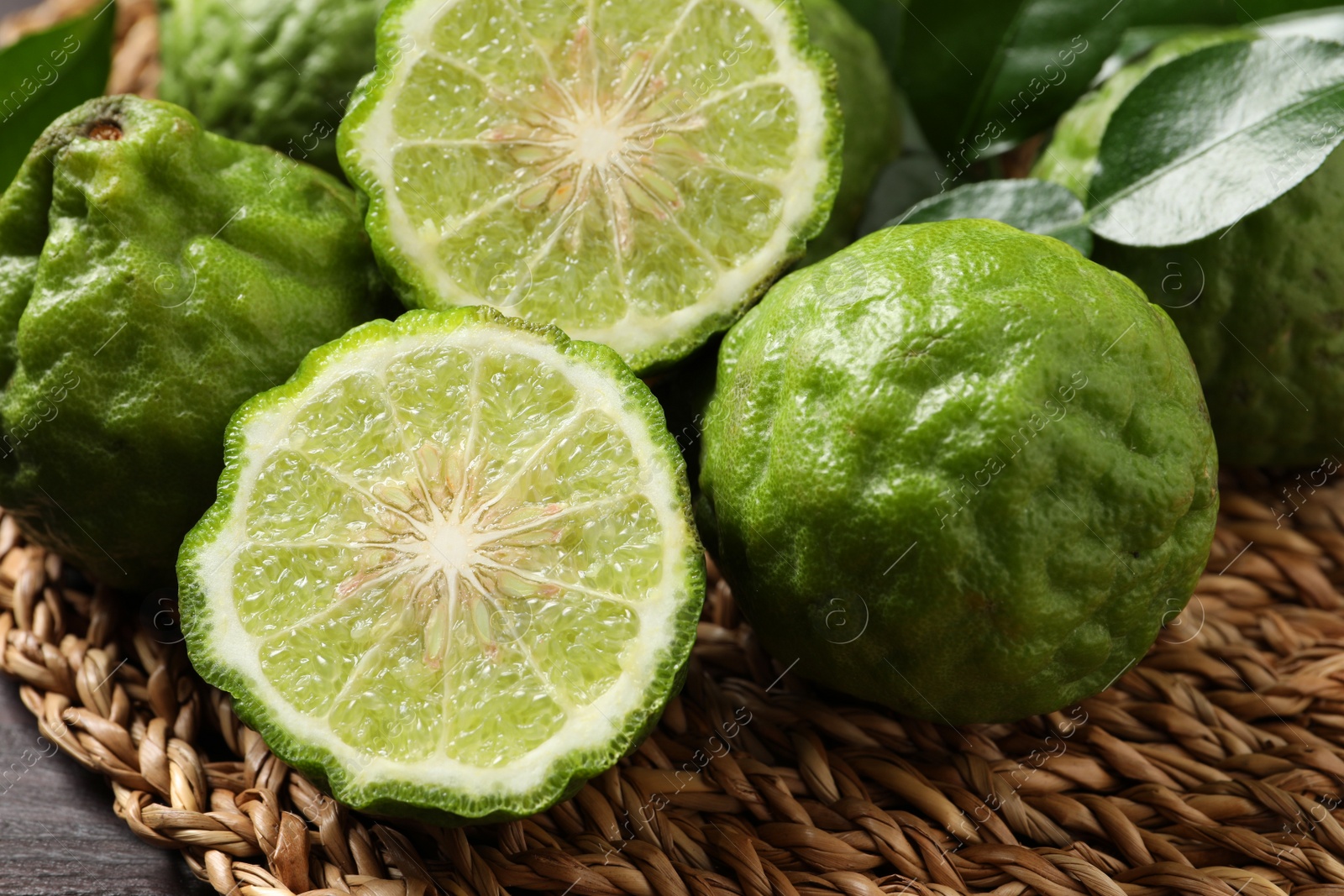 Photo of Whole and cut ripe bergamot fruits on wicker mat, closeup