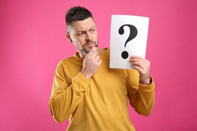 Photo of Emotional man holding paper with question mark on pink background