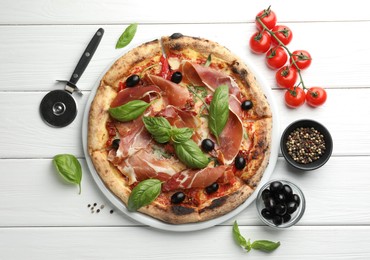 Tasty pizza with cured ham, olives, tomatoes and basil on white wooden table, flat lay