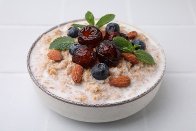 Photo of Tasty wheat porridge with milk, dates, blueberries and almonds in bowl on white table, closeup