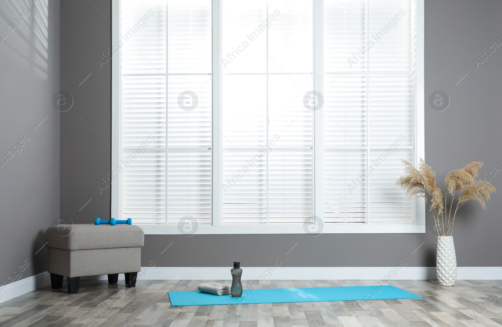 Photo of Exercise mat with dumbbells, bottle of water and pouf in spacious room