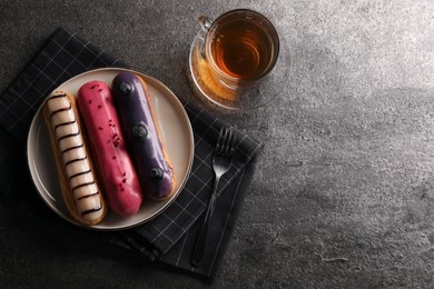 Different tasty glazed eclairs served with tea on grey textured table, flat lay. Space for text