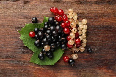Different fresh ripe currants and green leaf on wooden table, top view