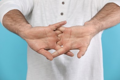Photo of Man cracking his knuckles on light blue background, closeup. Bad habit