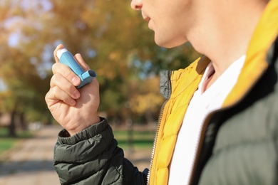 Photo of Man using asthma inhaler outdoors. Health care