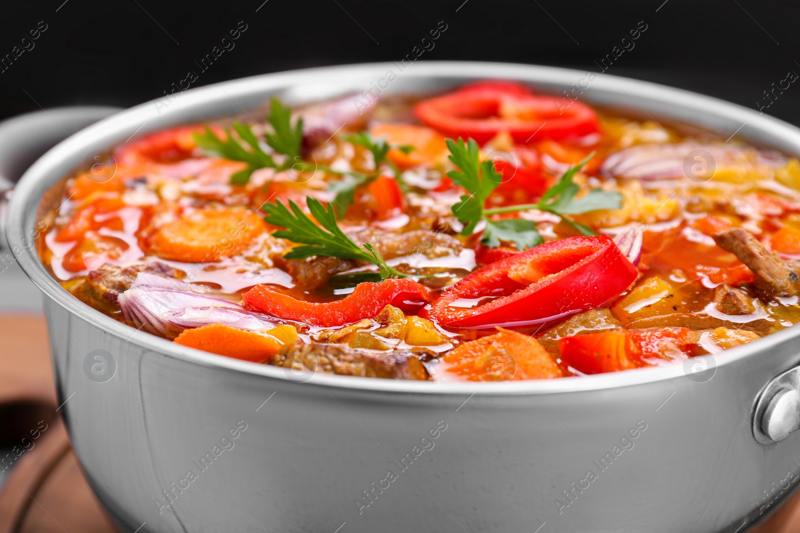 Photo of Saucepan of delicious vegetable soup with meat and ingredients on grey wooden table, closeup