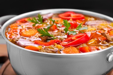 Saucepan of delicious vegetable soup with meat and ingredients on grey wooden table, closeup