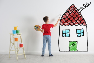 Cute child drawing house on white wall indoors