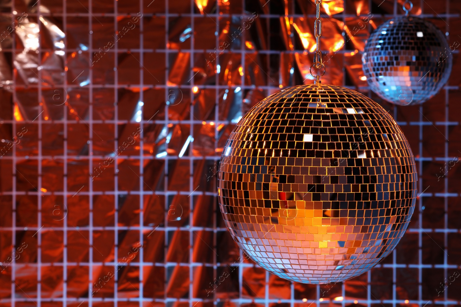 Photo of Shiny disco balls against foil party curtain under color lights, space for text