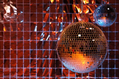 Photo of Shiny disco balls against foil party curtain under color lights, space for text