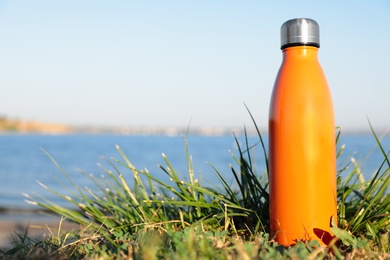 Modern orange thermos bottle on beach. Space for text