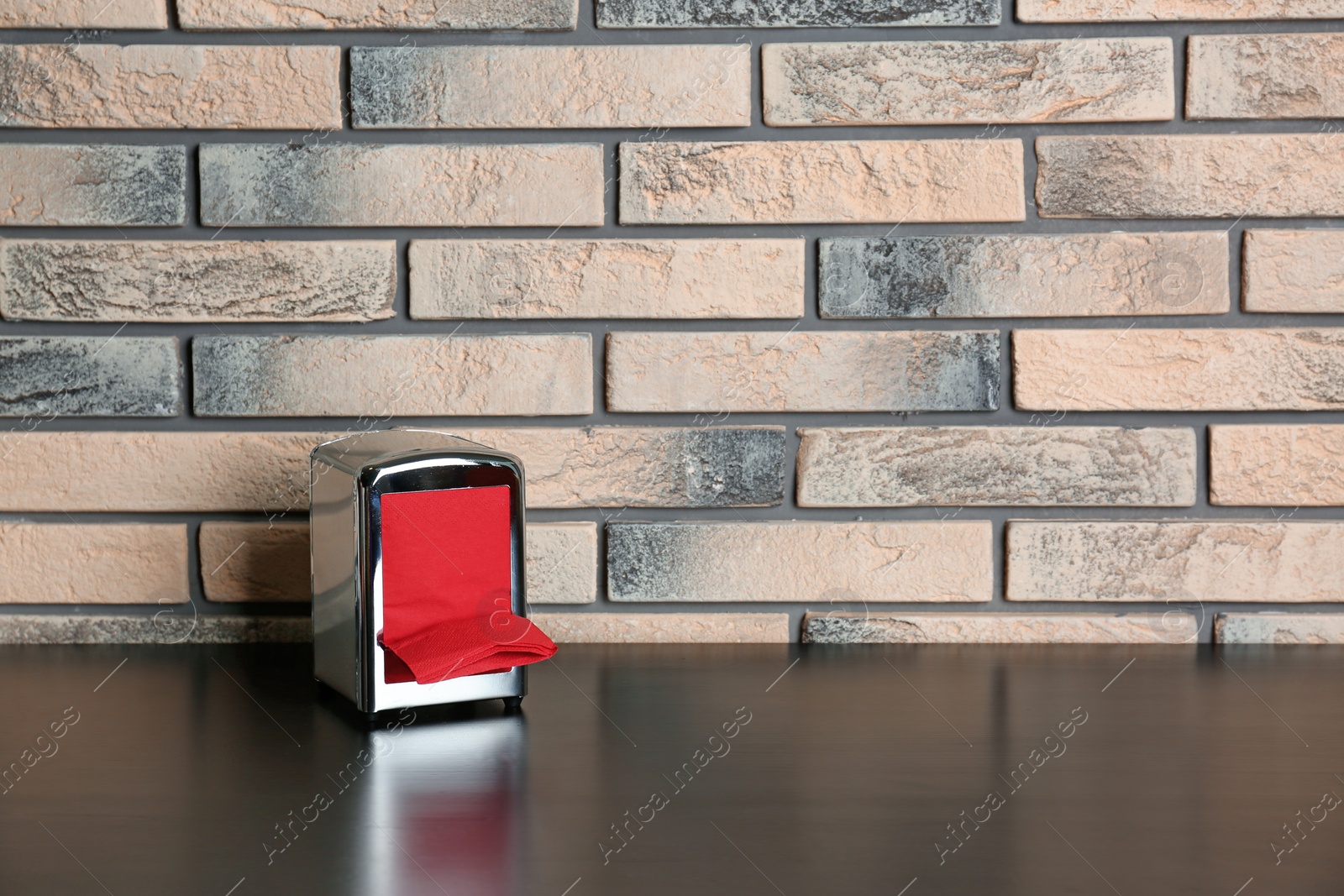 Photo of Napkin holder with paper serviettes on table near brick wall. Space for text