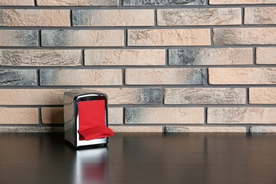 Photo of Napkin holder with paper serviettes on table near brick wall. Space for text