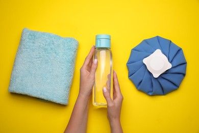 Woman with bottle of water, cold compress and towel on yellow background, top view. Heat stroke treatment