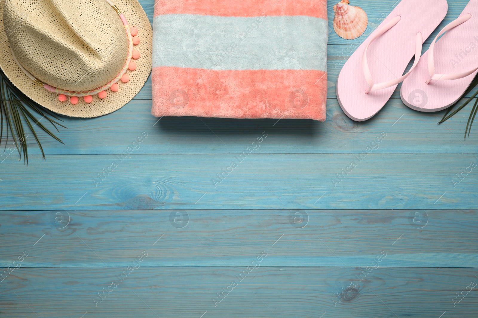 Photo of Beach towel, straw hat and flip flops on light blue wooden background, flat lay. Space for text