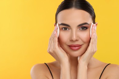 Photo of Beautiful woman removing makeup with cotton pads on orange background. Space for text