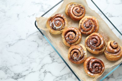 Photo of Baking dish with tasty cinnamon rolls on white marble table, top view. Space for text