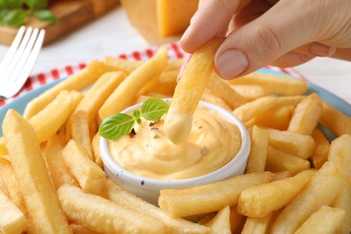 Photo of Woman dipping delicious French fries into cheese sauce, closeup