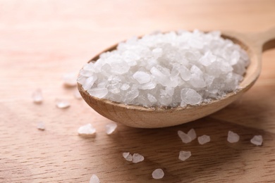 Photo of Spoon with white sea salt on wooden table, closeup. Spa treatment