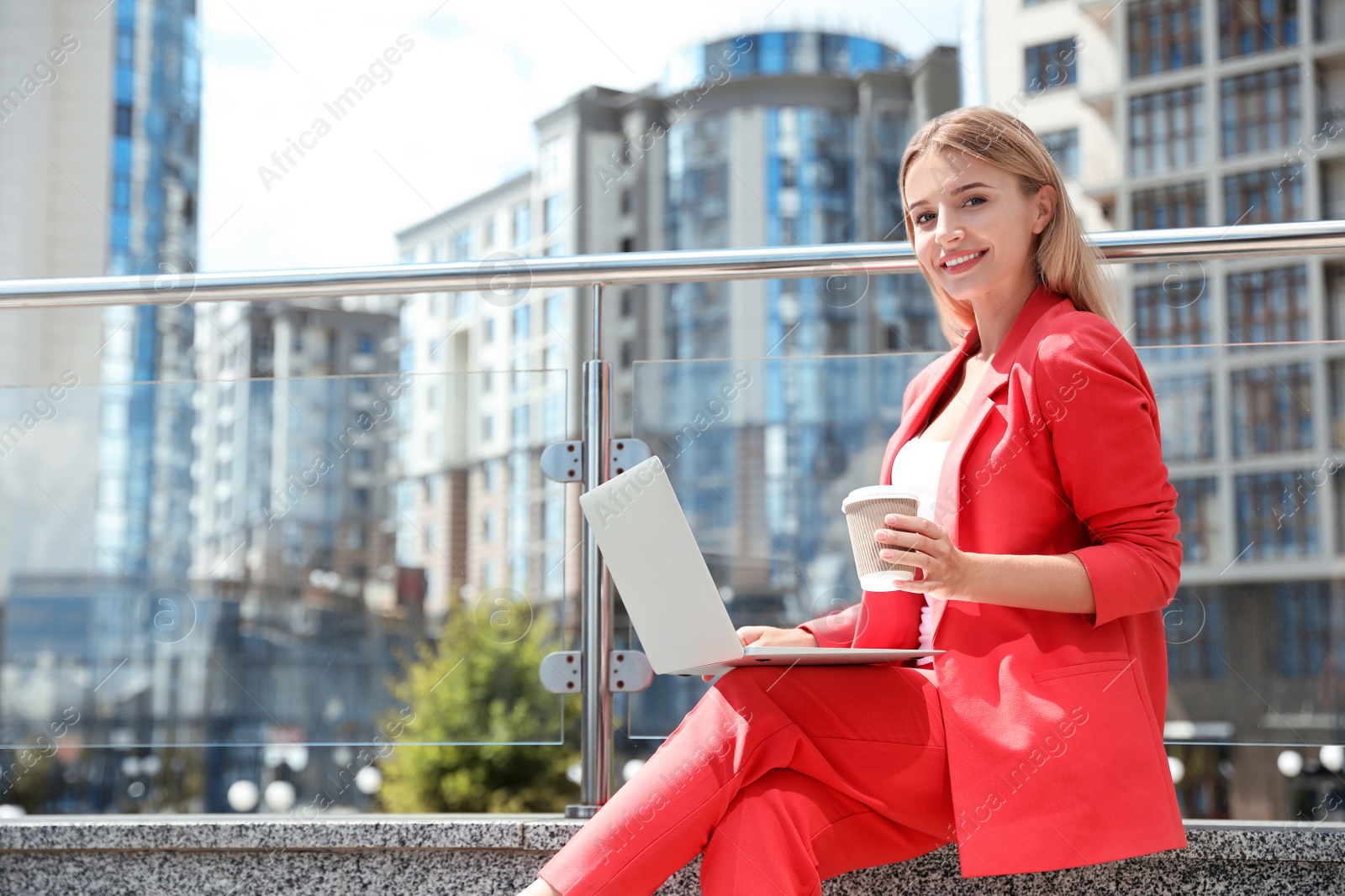 Photo of Beautiful businesswoman with laptop and cup of coffee on city street. Space for text