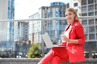 Photo of Beautiful businesswoman with laptop and cup of coffee on city street. Space for text