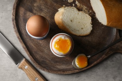 Photo of Fresh soft boiled eggs in cups and bread on grey table, flat lay