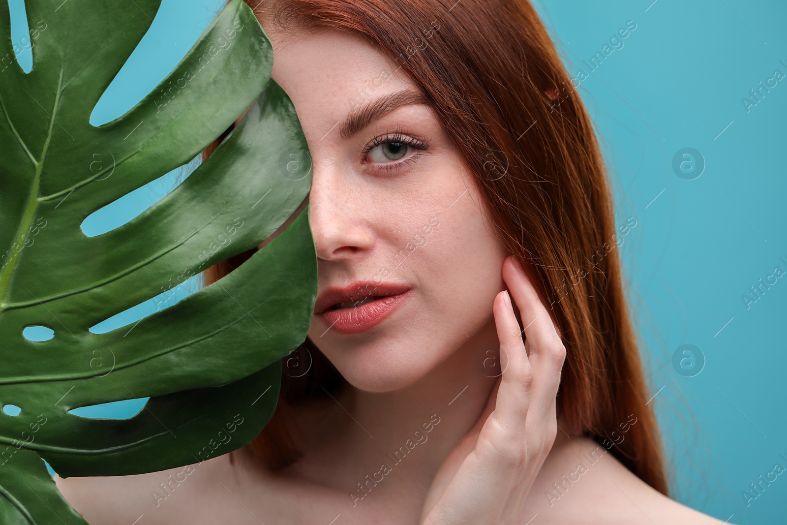 Photo of Beautiful woman with freckles and monstera leaf on light blue background, closeup