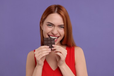 Young woman eating tasty chocolate on purple background