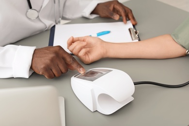 Photo of Young African-American doctor checking patient's blood pressure in hospital