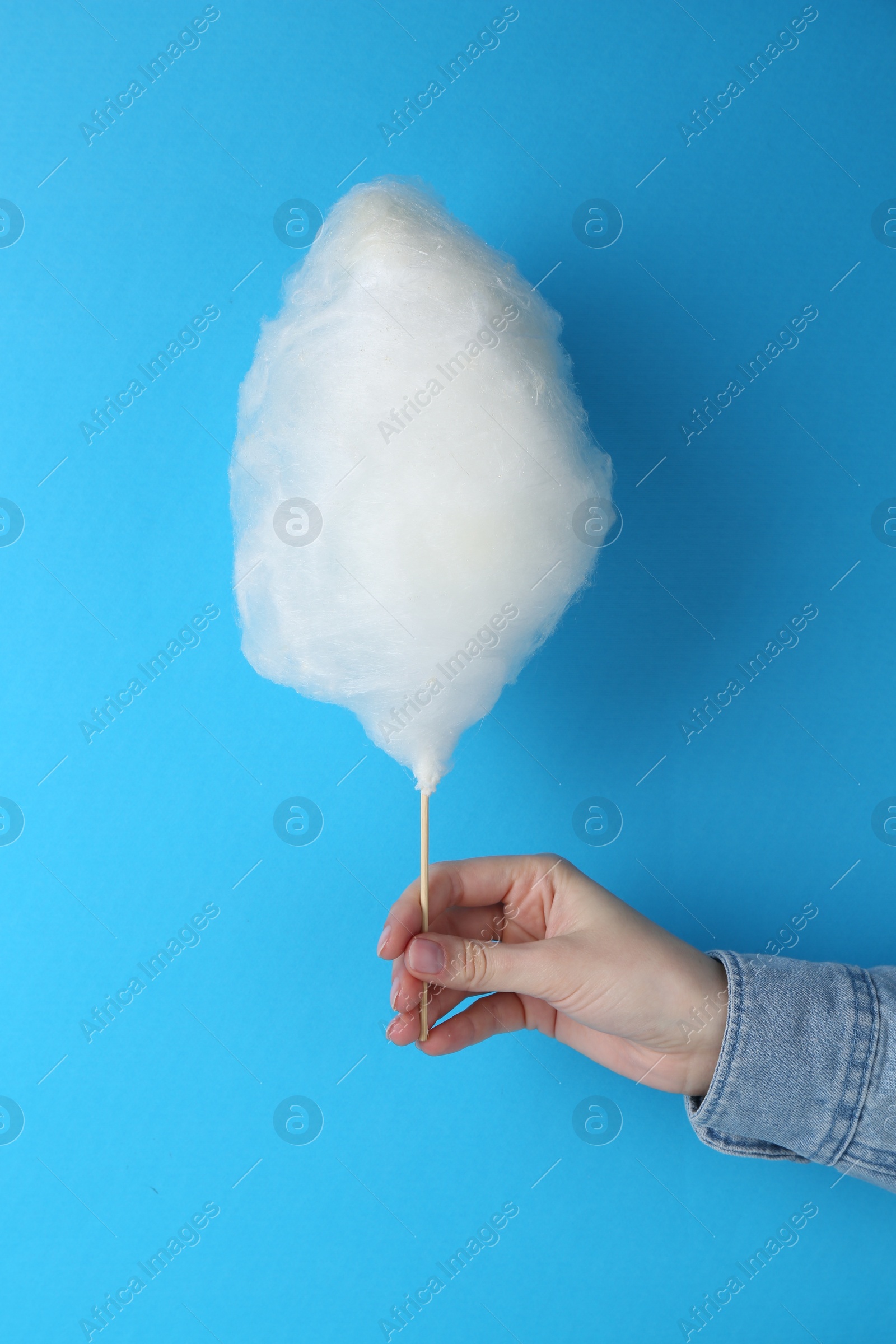 Photo of Woman holding sweet cotton candy on light blue background, closeup